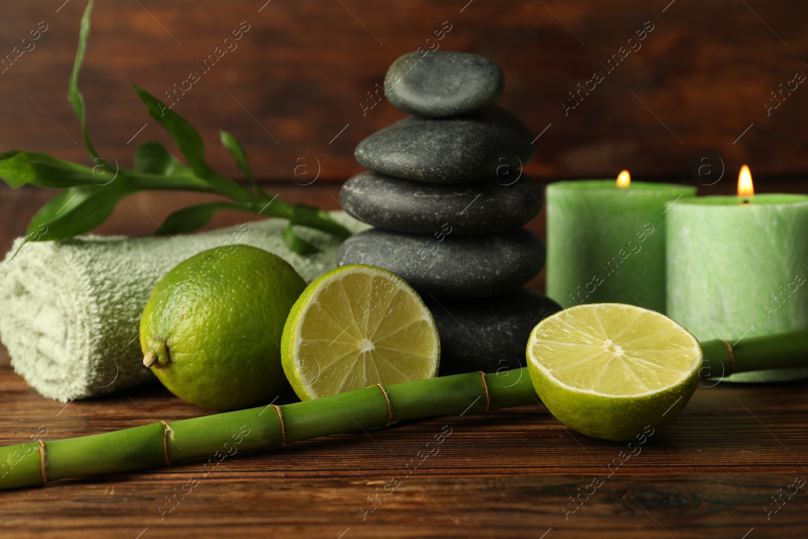 Spa composition with fresh limes, pebble stones, burning candles and bamboo on wooden table, closeup Photo of Spa composition with fresh limes, pebble stones, burning candles and bamboo on wooden table, closeup