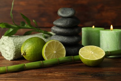 Photo of Spa composition with fresh limes, pebble stones, burning candles and bamboo on wooden table, closeup