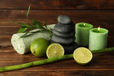 Photo of Spa composition with fresh limes, pebble stones, burning candles and bamboo on wooden table