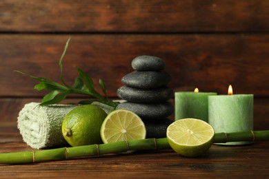 Photo of Spa composition with fresh limes, pebble stones, burning candles and bamboo on wooden table