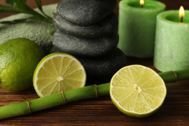 Photo of Spa composition with fresh limes, pebble stones and bamboo on wooden table, closeup