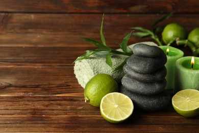Photo of Spa composition with fresh limes, pebble stones and burning candles on wooden table, closeup. Space for text