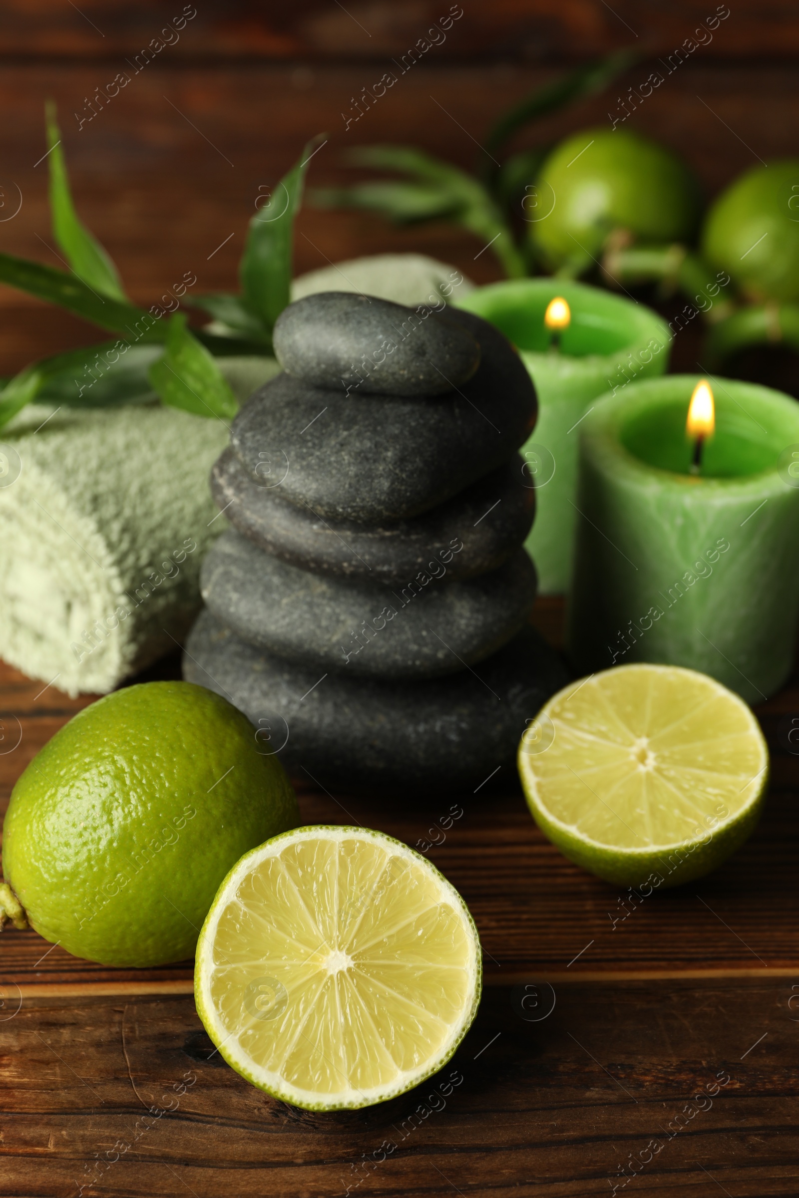 Spa composition with fresh limes, pebble stones and burning candles on wooden table, closeup Photo of Spa composition with fresh limes, pebble stones and burning candles on wooden table, closeup
