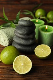 Photo of Spa composition with fresh limes, pebble stones and burning candles on wooden table, closeup