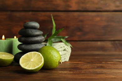 Photo of Spa composition with fresh limes, pebble stones and burning candles on wooden table, closeup. Space for text
