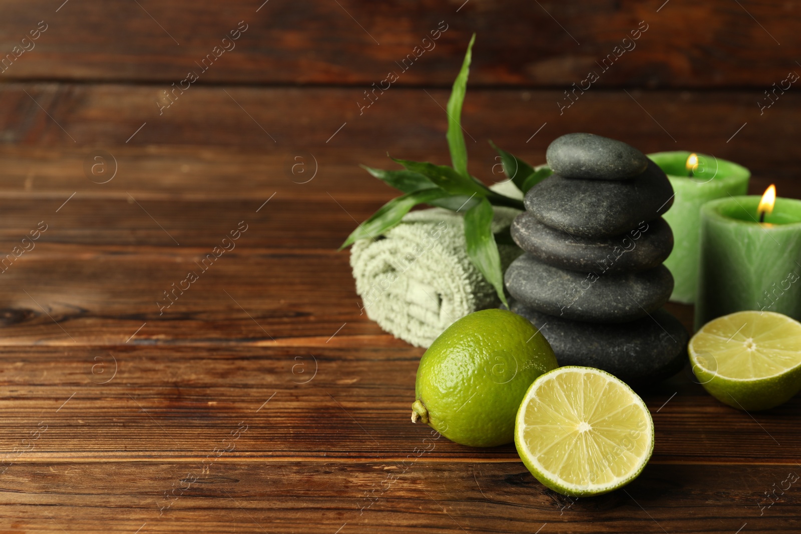 Spa composition with fresh limes, pebble stones and burning candles on wooden table, closeup. Space for text Photo of Spa composition with fresh limes, pebble stones and burning candles on wooden table, closeup. Space for text