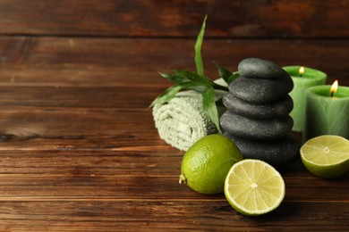 Photo of Spa composition with fresh limes, pebble stones and burning candles on wooden table, closeup. Space for text