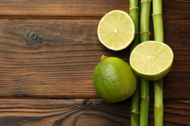 Photo of Fresh limes and bamboo stems on wooden table, flat lay. Space for text