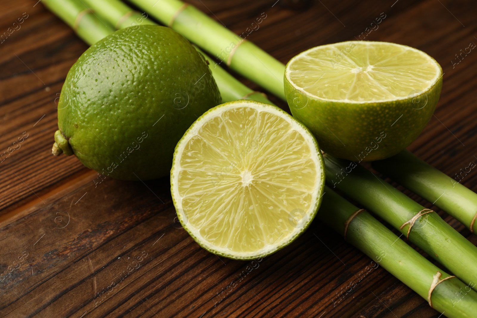 Fresh limes and bamboo stems on wooden table, closeup Photo of Fresh limes and bamboo stems on wooden table, closeup