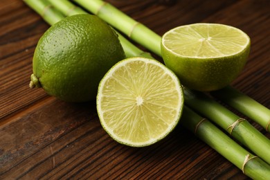 Photo of Fresh limes and bamboo stems on wooden table, closeup