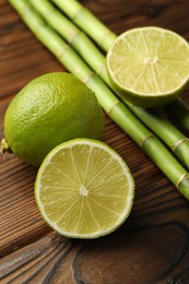 Photo of Fresh limes and bamboo stems on wooden table, closeup