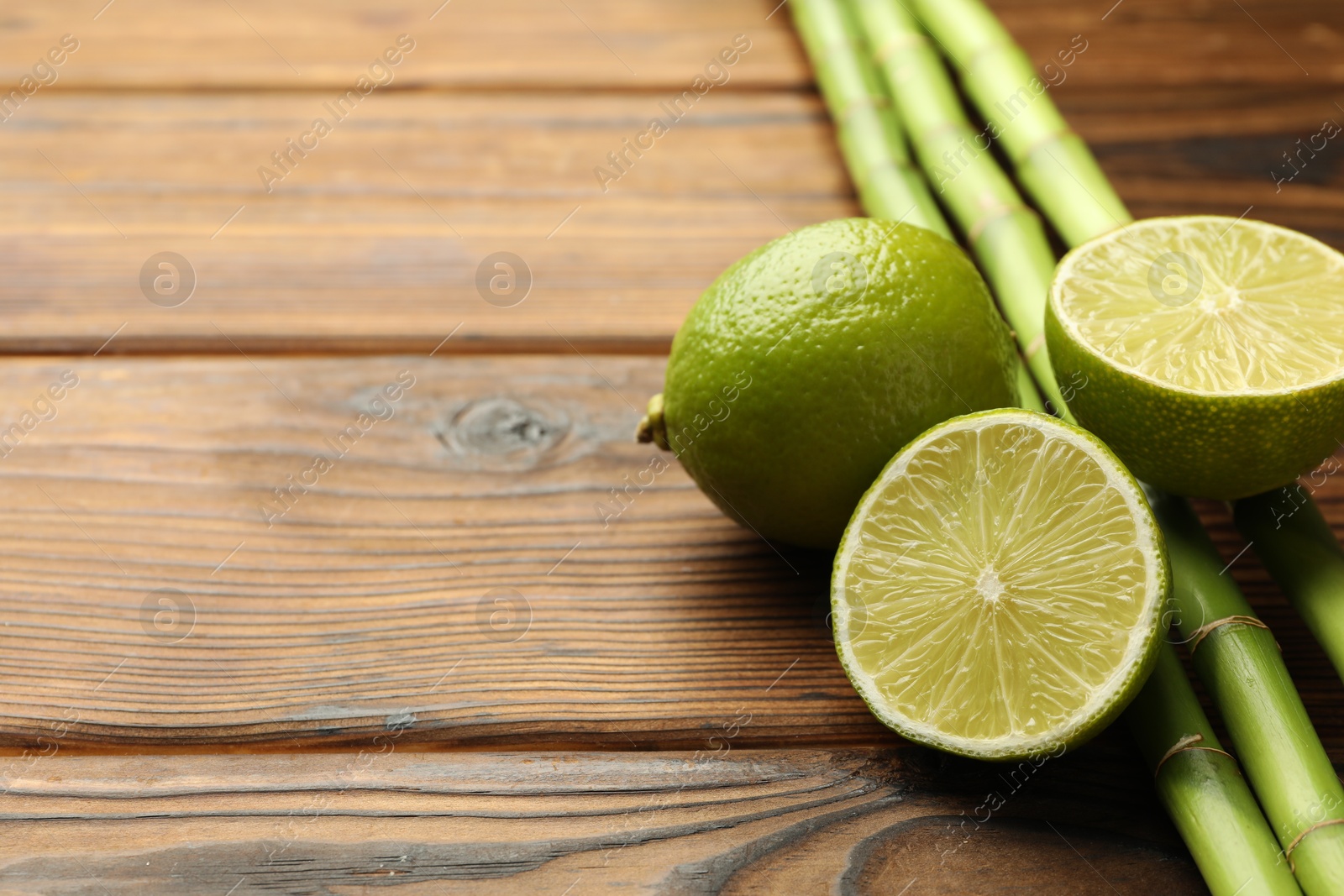 Fresh limes and bamboo stems on wooden table, closeup. Space for text Photo of Fresh limes and bamboo stems on wooden table, closeup. Space for text