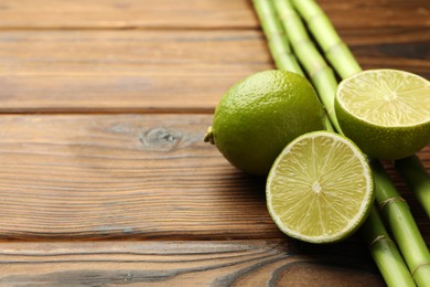 Photo of Fresh limes and bamboo stems on wooden table, closeup. Space for text