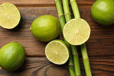 Photo of Fresh limes and bamboo stems on wooden table, flat lay