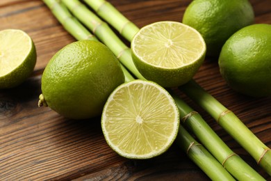 Photo of Fresh limes and bamboo stems on wooden table, closeup