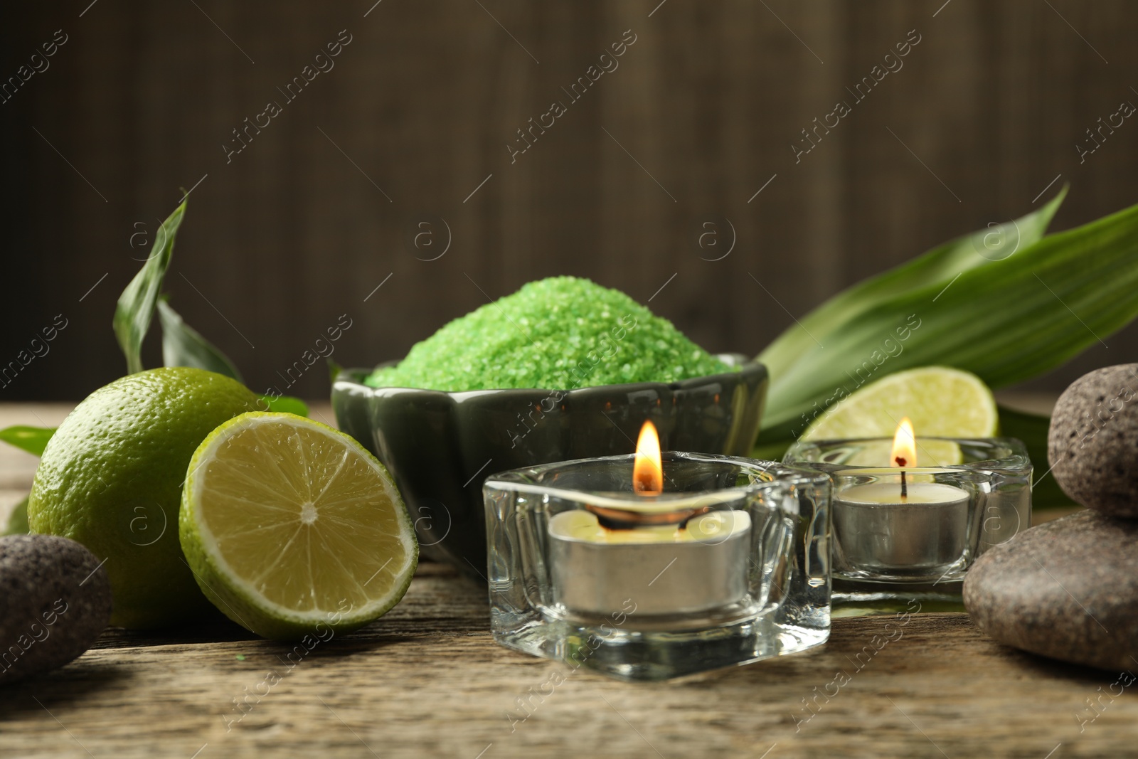 Photo of Spa composition with fresh limes, sea salt and burning candles on wooden table, closeup