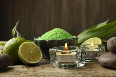 Photo of Spa composition with fresh limes, sea salt and burning candles on wooden table, closeup