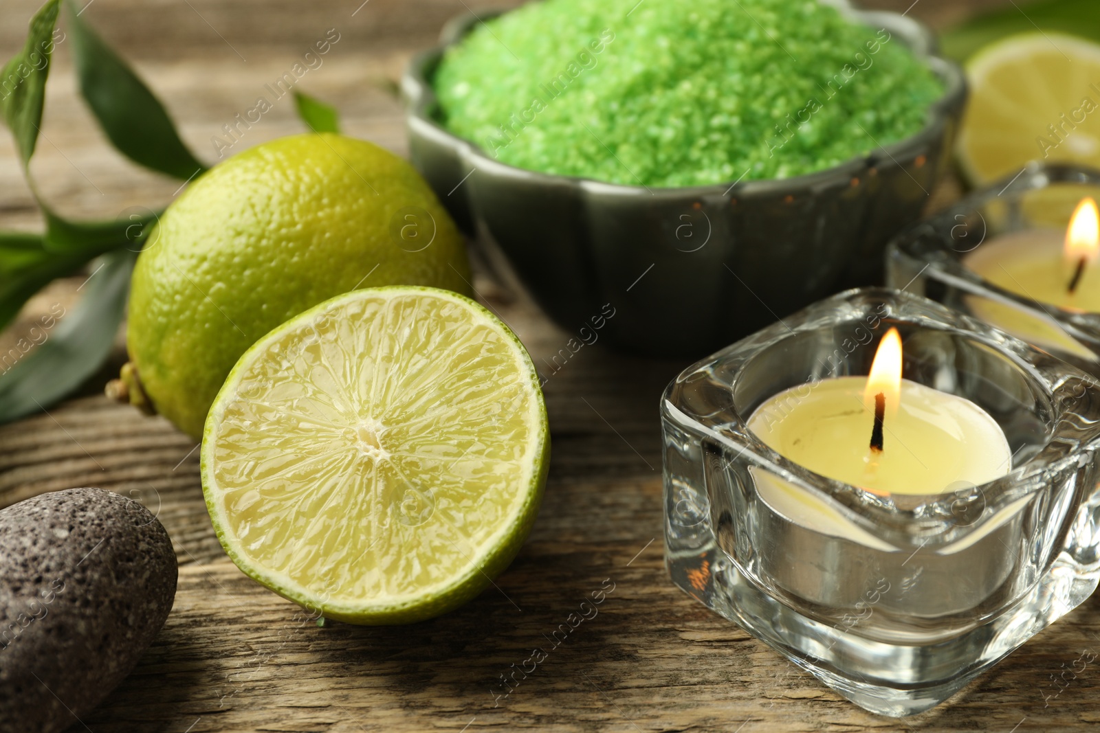 Photo of Spa composition with fresh limes, sea salt and burning candles on wooden table, closeup