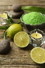 Photo of Spa composition with fresh limes, sea salt and burning candles on wooden table, closeup
