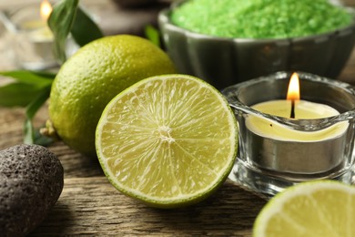 Photo of Spa composition with fresh limes, sea salt and burning candle on wooden table, closeup