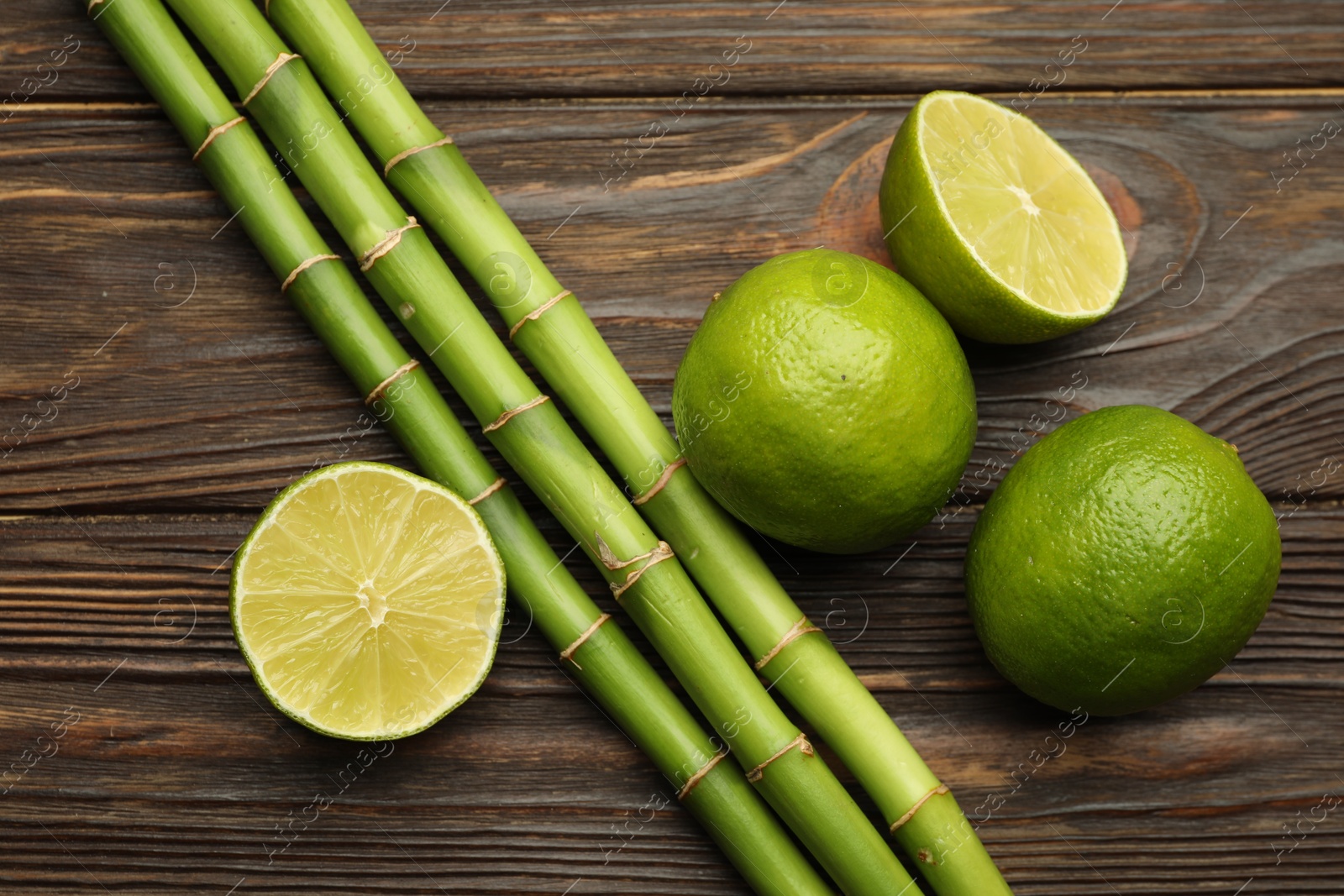 Photo of Fresh limes and bamboo stems on wooden table, flat lay