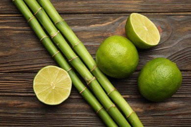 Photo of Fresh limes and bamboo stems on wooden table, flat lay