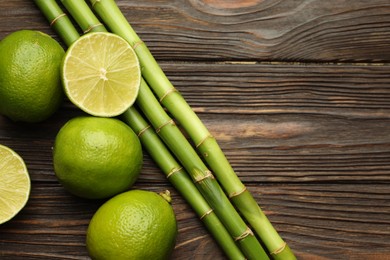 Photo of Fresh limes and bamboo stems on wooden table, flat lay. Space for text