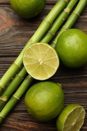 Photo of Fresh limes and bamboo stems on wooden table, flat lay
