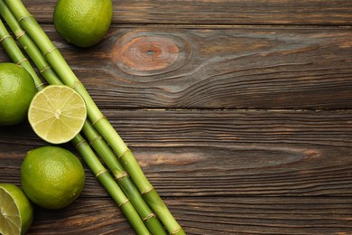 Photo of Fresh limes and bamboo stems on wooden table, flat lay. Space for text