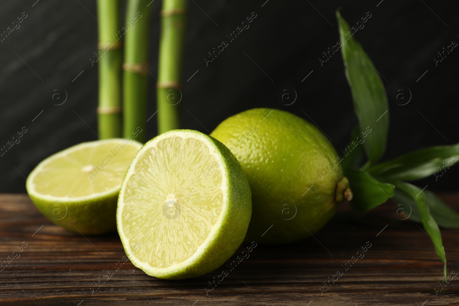 Fresh limes and bamboo leaves on wooden table against dark background, closeup Photo of Fresh limes and bamboo leaves on wooden table against dark background, closeup