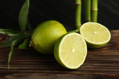 Photo of Fresh limes and bamboo leaves on wooden table against dark background, closeup