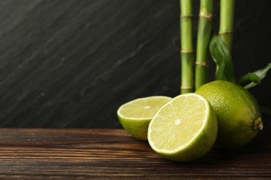 Photo of Fresh limes on wooden table against dark background, closeup. Space for text