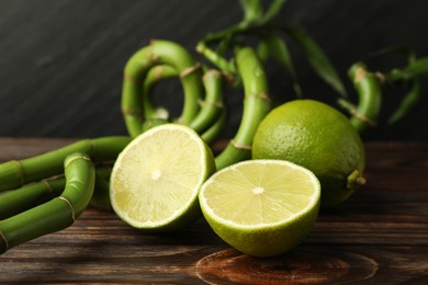 Photo of Fresh limes and bamboo stems on wooden table against dark background, closeup