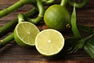 Photo of Fresh limes, bamboo leaves and stems on wooden table, closeup