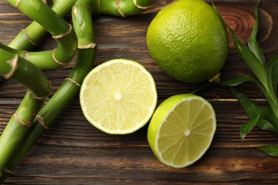Photo of Fresh limes, bamboo leaves and stems on wooden table, flat lay