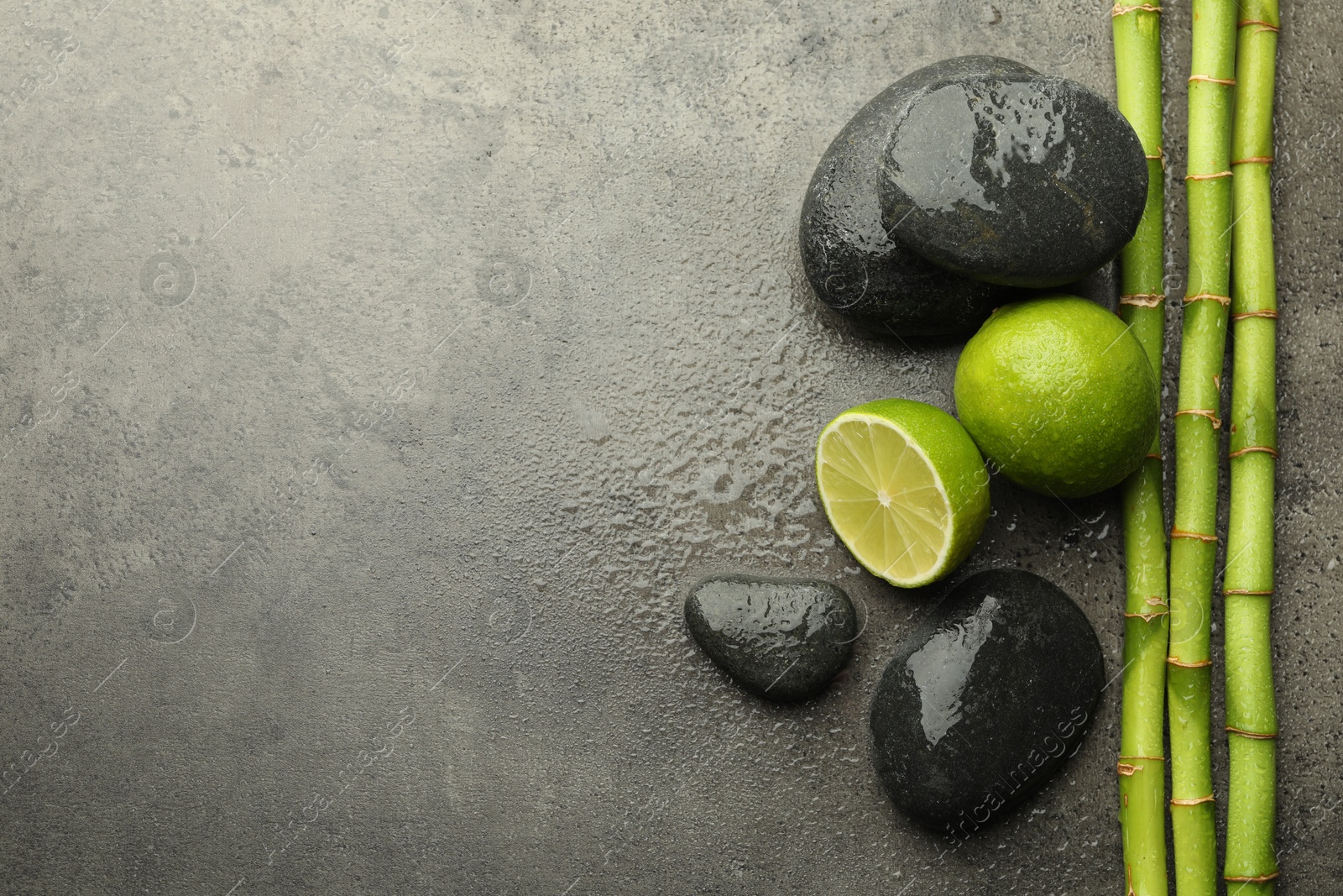 Spa composition with wet limes, pebble stones and bamboo stems on grey table, flat lay. Space for text Photo of Spa composition with wet limes, pebble stones and bamboo stems on grey table, flat lay. Space for text