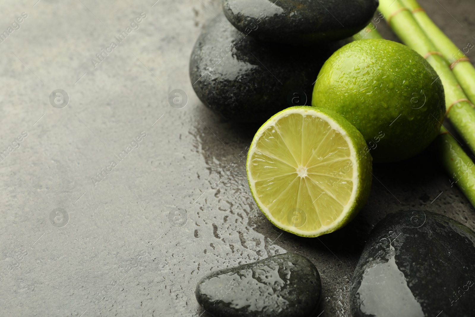 Spa composition with wet limes, pebble stones and bamboo stems on grey table, closeup. Space for text Photo of Spa composition with wet limes, pebble stones and bamboo stems on grey table, closeup. Space for text