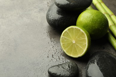 Photo of Spa composition with wet limes, pebble stones and bamboo stems on grey table, closeup. Space for text