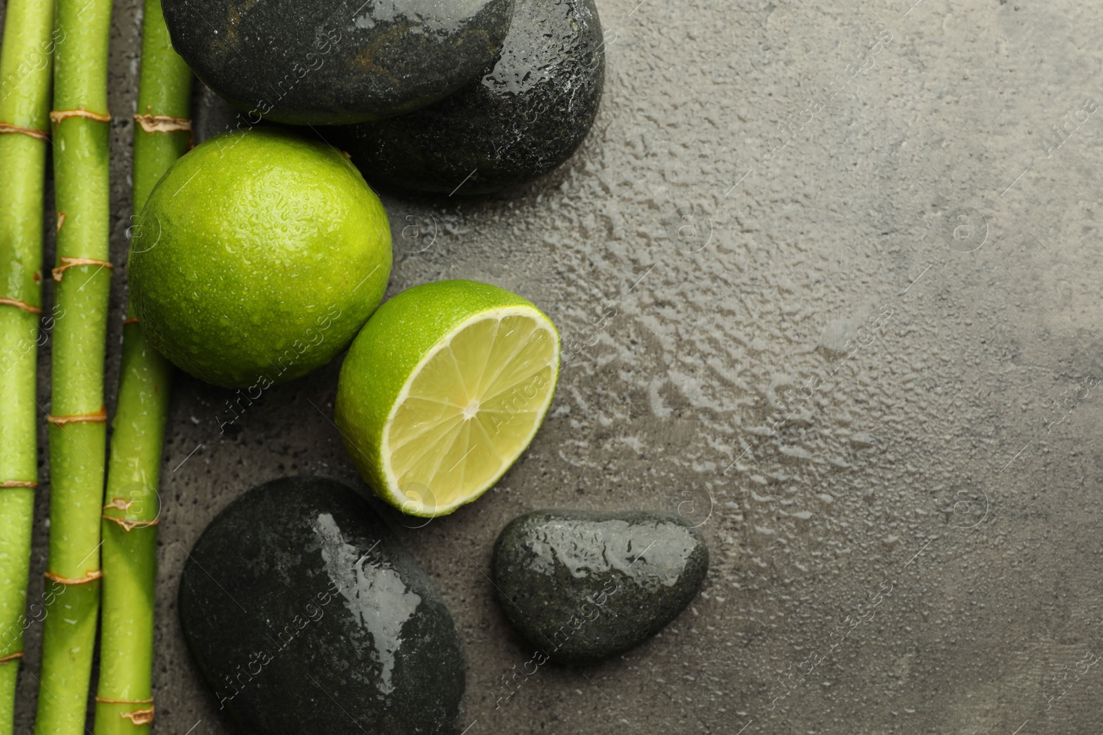 Spa composition with wet limes, pebble stones and bamboo stems on grey table, flat lay. Space for text Photo of Spa composition with wet limes, pebble stones and bamboo stems on grey table, flat lay. Space for text