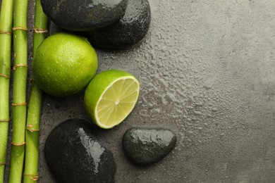 Photo of Spa composition with wet limes, pebble stones and bamboo stems on grey table, flat lay. Space for text