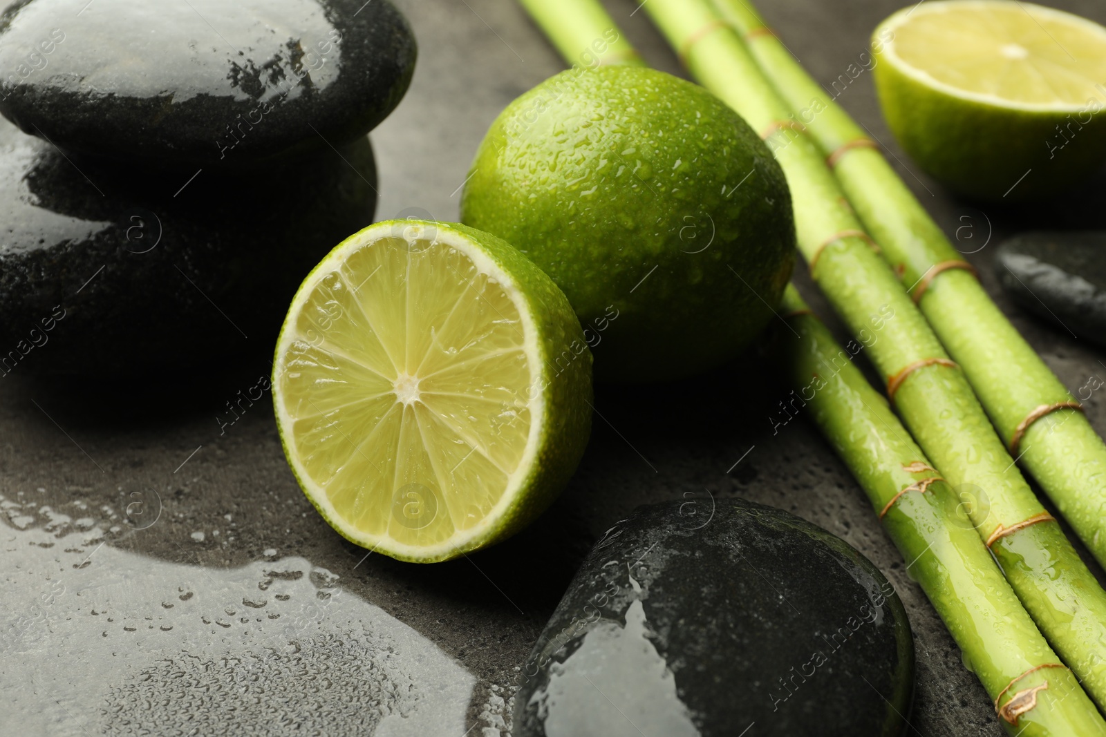 Photo of Spa composition with wet limes, pebble stones and bamboo stems on grey table, closeup