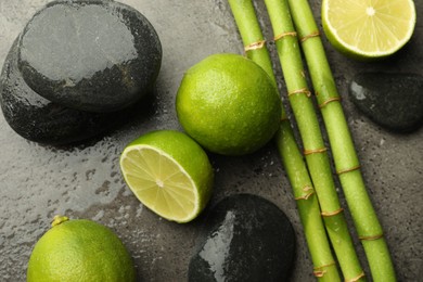 Photo of Spa composition with wet limes, pebble stones and bamboo stems on grey table, flat lay