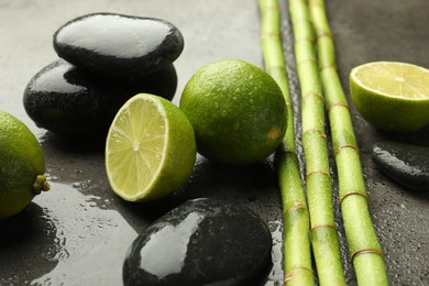 Photo of Spa composition with wet limes, pebble stones and bamboo stems on grey table, closeup
