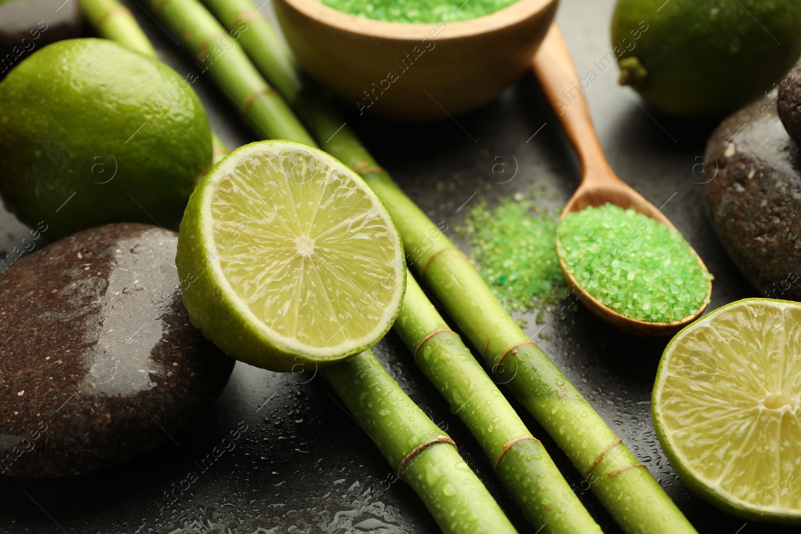 Photo of Spa composition with wet limes, sea salt, pebble stones and bamboo stems on grey table, closeup