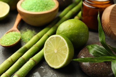 Photo of Spa composition with wet limes, sea salt, pebble stone and bamboo on grey table, closeup