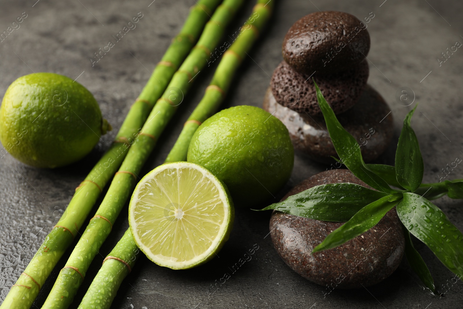 Spa composition with wet limes, pebble stones, bamboo leaves and stems on grey table, closeup Photo of Spa composition with wet limes, pebble stones, bamboo leaves and stems on grey table, closeup