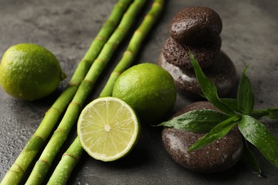 Photo of Spa composition with wet limes, pebble stones, bamboo leaves and stems on grey table, closeup