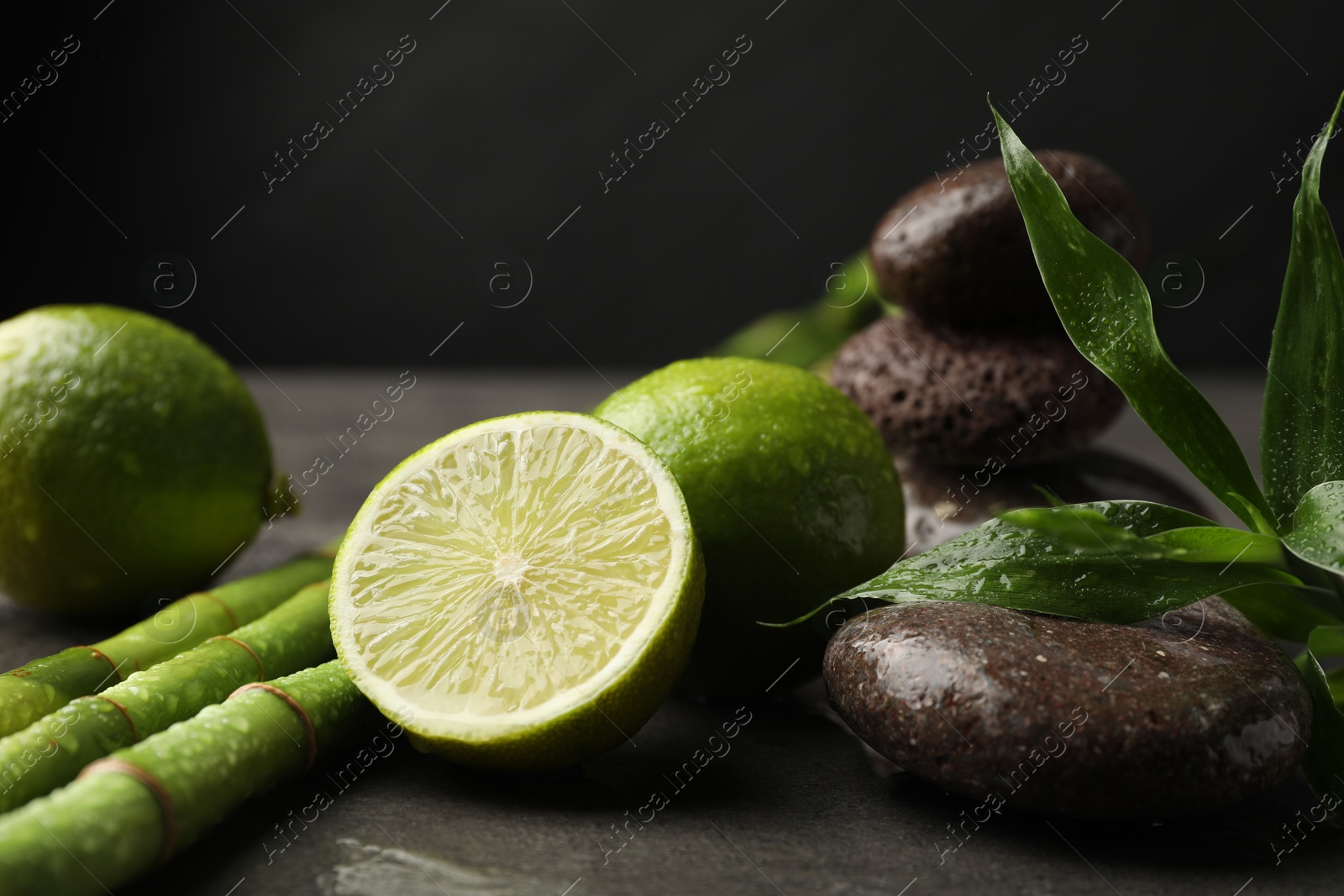 Spa composition with wet limes, pebble stones, bamboo leaves and stems on grey table against black background, closeup Photo of Spa composition with wet limes, pebble stones, bamboo leaves and stems on grey table against black background, closeup