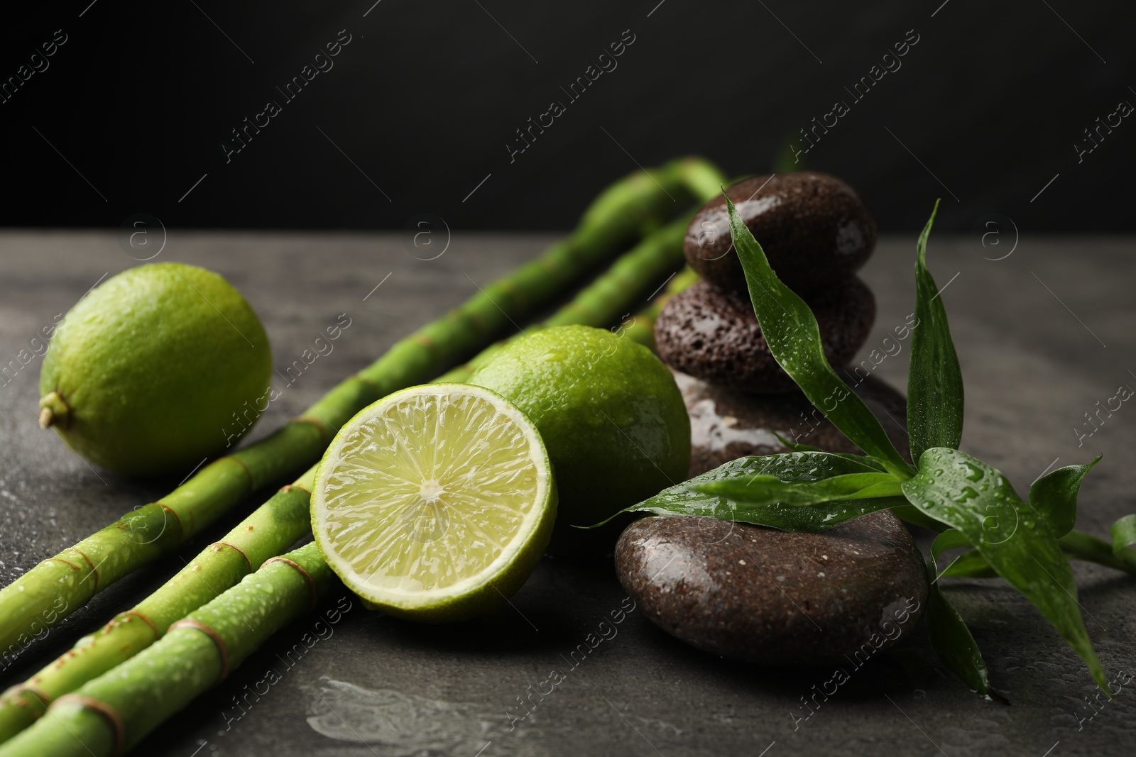 Spa composition with wet limes, pebble stones, bamboo leaves and stems on grey table against black background, closeup Photo of Spa composition with wet limes, pebble stones, bamboo leaves and stems on grey table against black background, closeup
