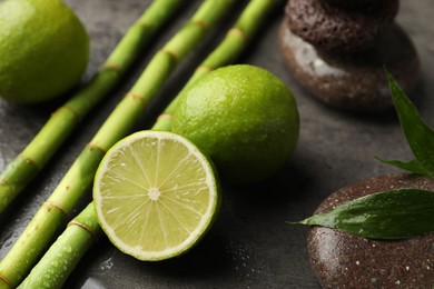Photo of Spa composition with wet limes, pebble stones, bamboo leaves and stems on grey table, closeup